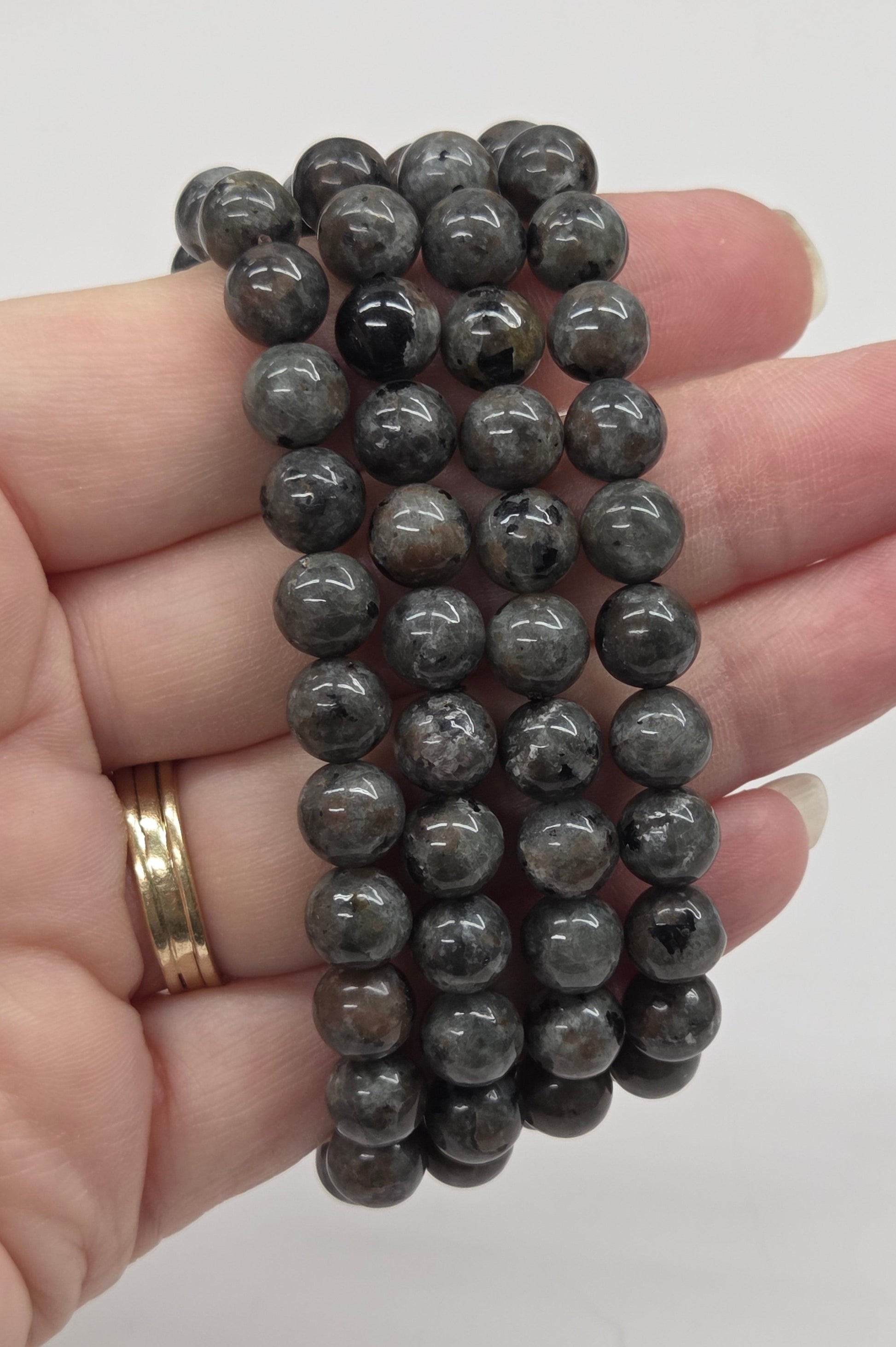 Hand holding multiple gray beaded bracelets against a white background