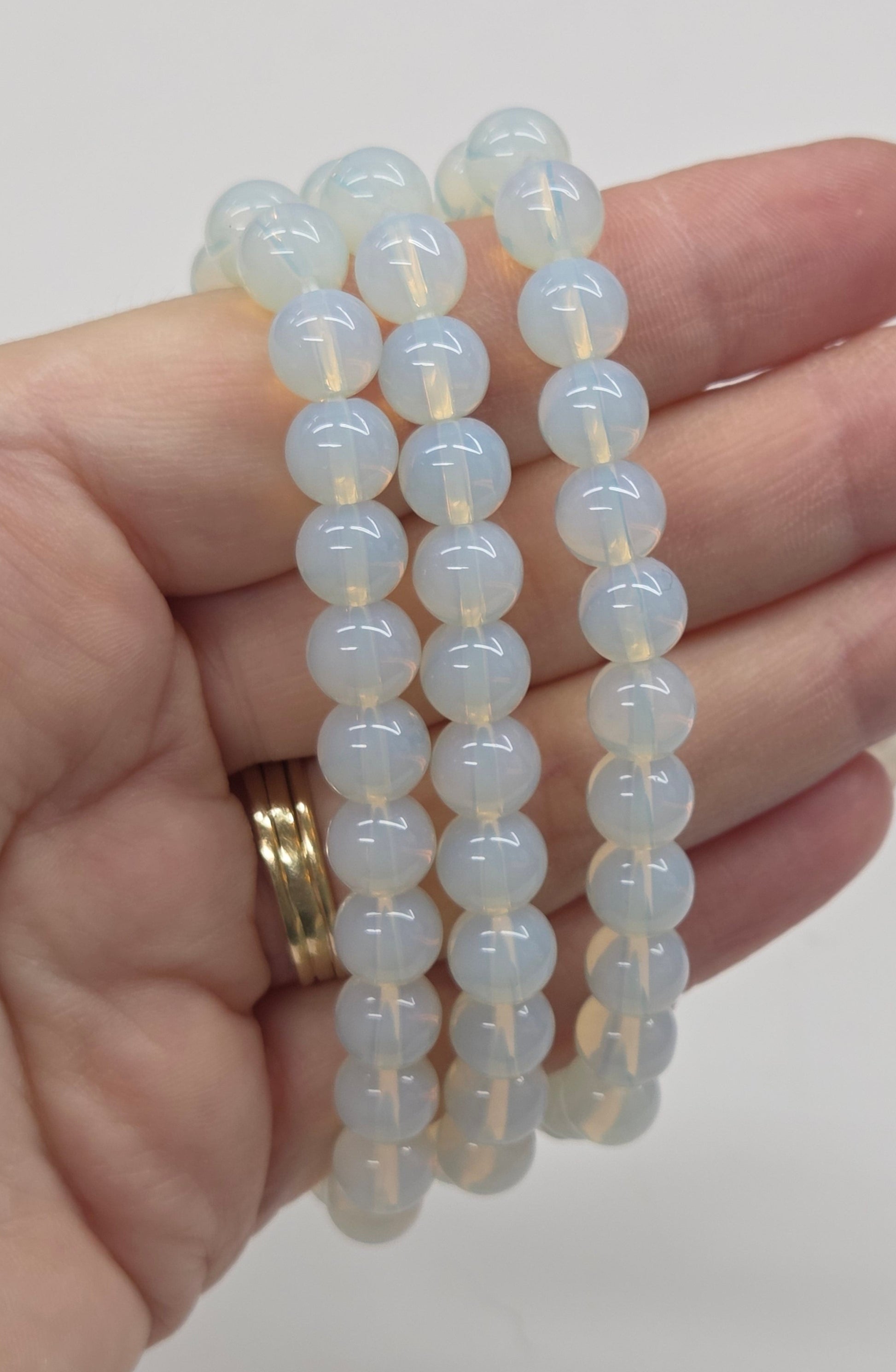 Hand wearing white beaded bracelets on a plain background