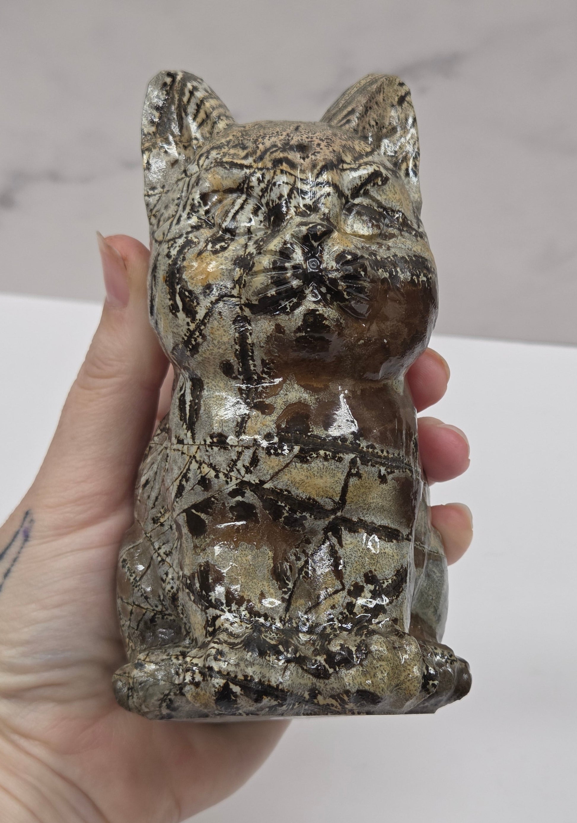 Hand holding a decorative Picture Jasper cat carving on a white background