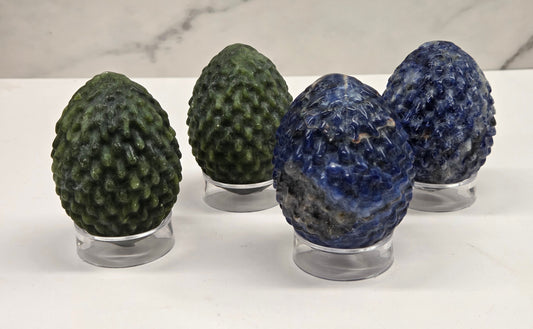 Green and blue dragon egg carvings on acrylic stands against a neutral background