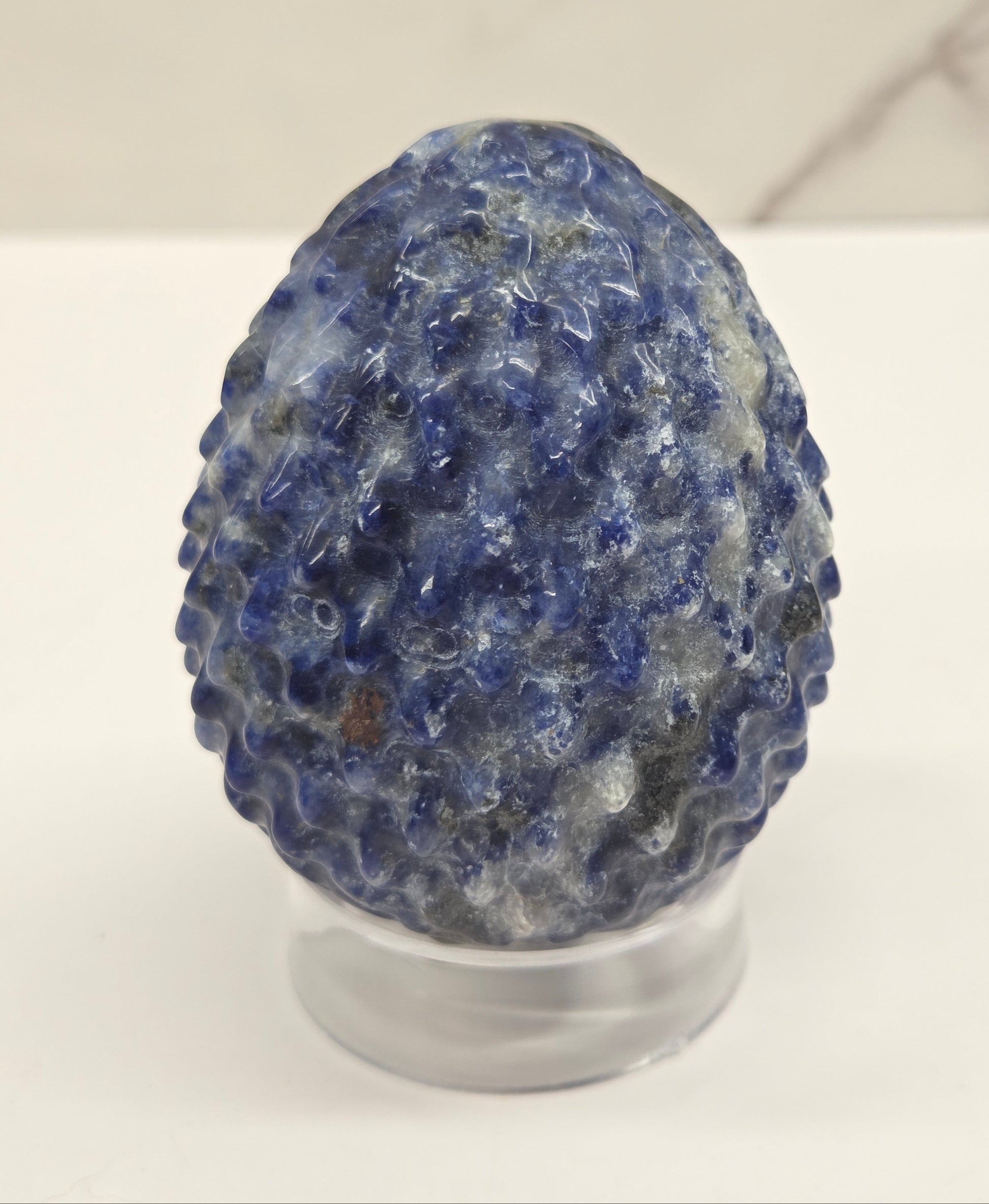 Sodalite dragon egg carving on an acrylic stand against a neutral background
