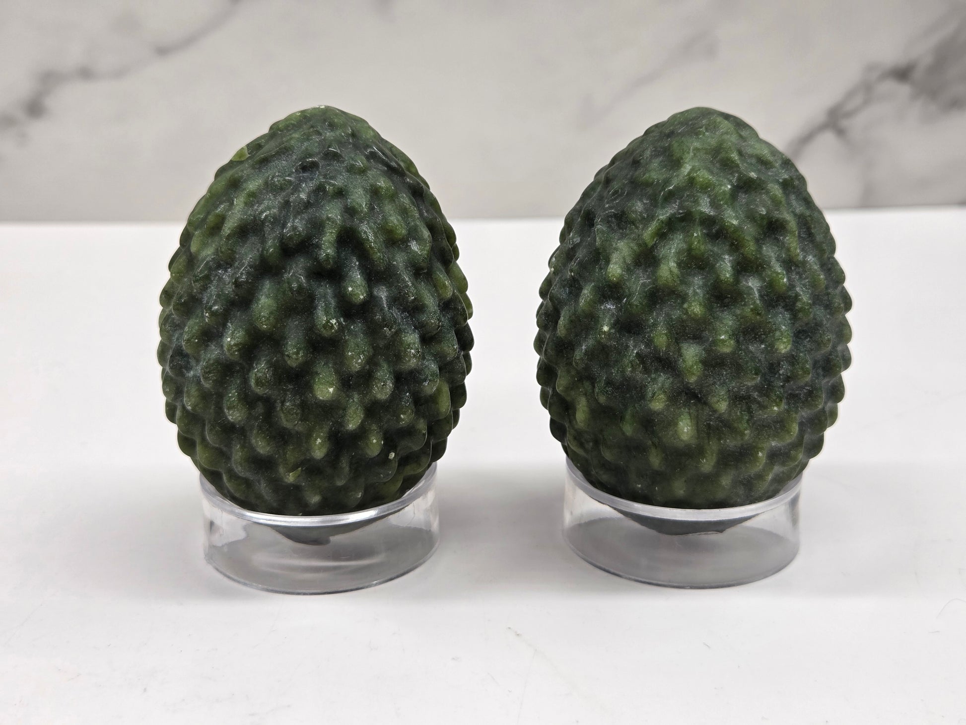 Green Jade dragon egg carvings on acrylic stands against a neutral background