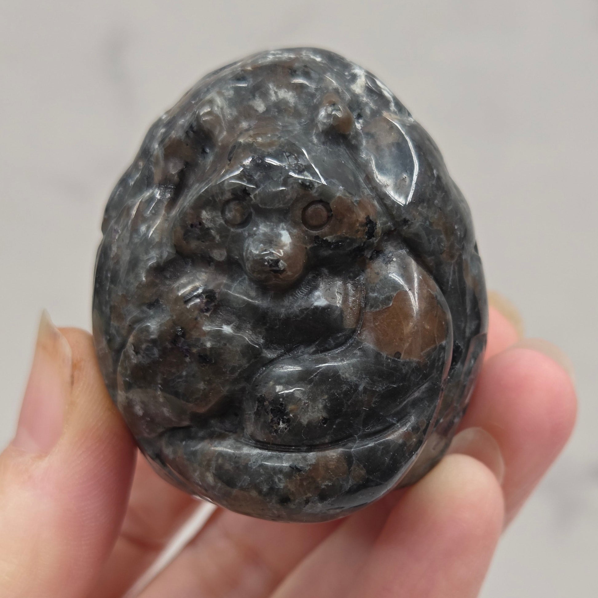 Hand holding a dark stone object with intricate carvings against a neutral background