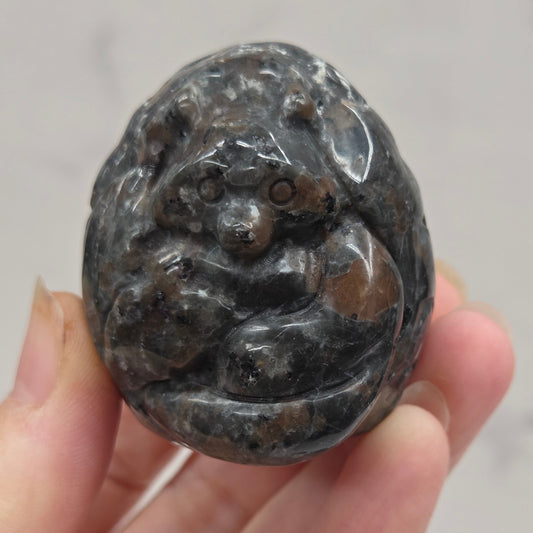 Hand holding a dark stone object with intricate carvings against a neutral background