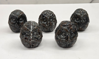 Five dark brown decorative owl figurines on a white surface with a marble background