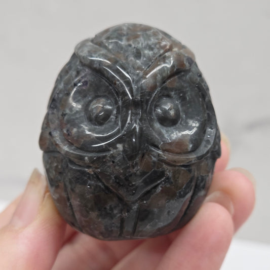 Hand holding a dark stone with carvings against a neutral background