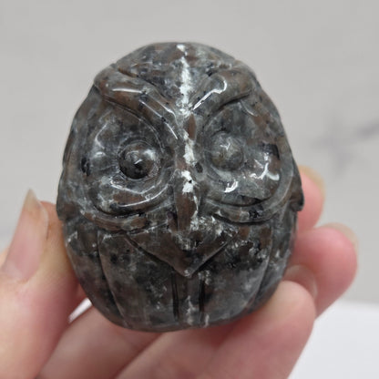 Hand holding a dark stone with intricate carvings against a plain background
