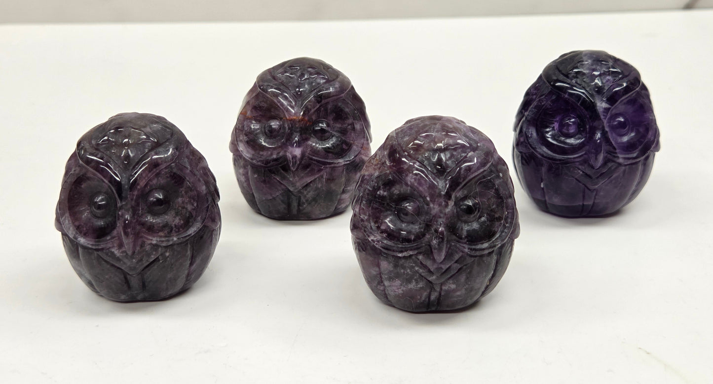 Four purple owl-shaped objects on a white surface with a marble background
