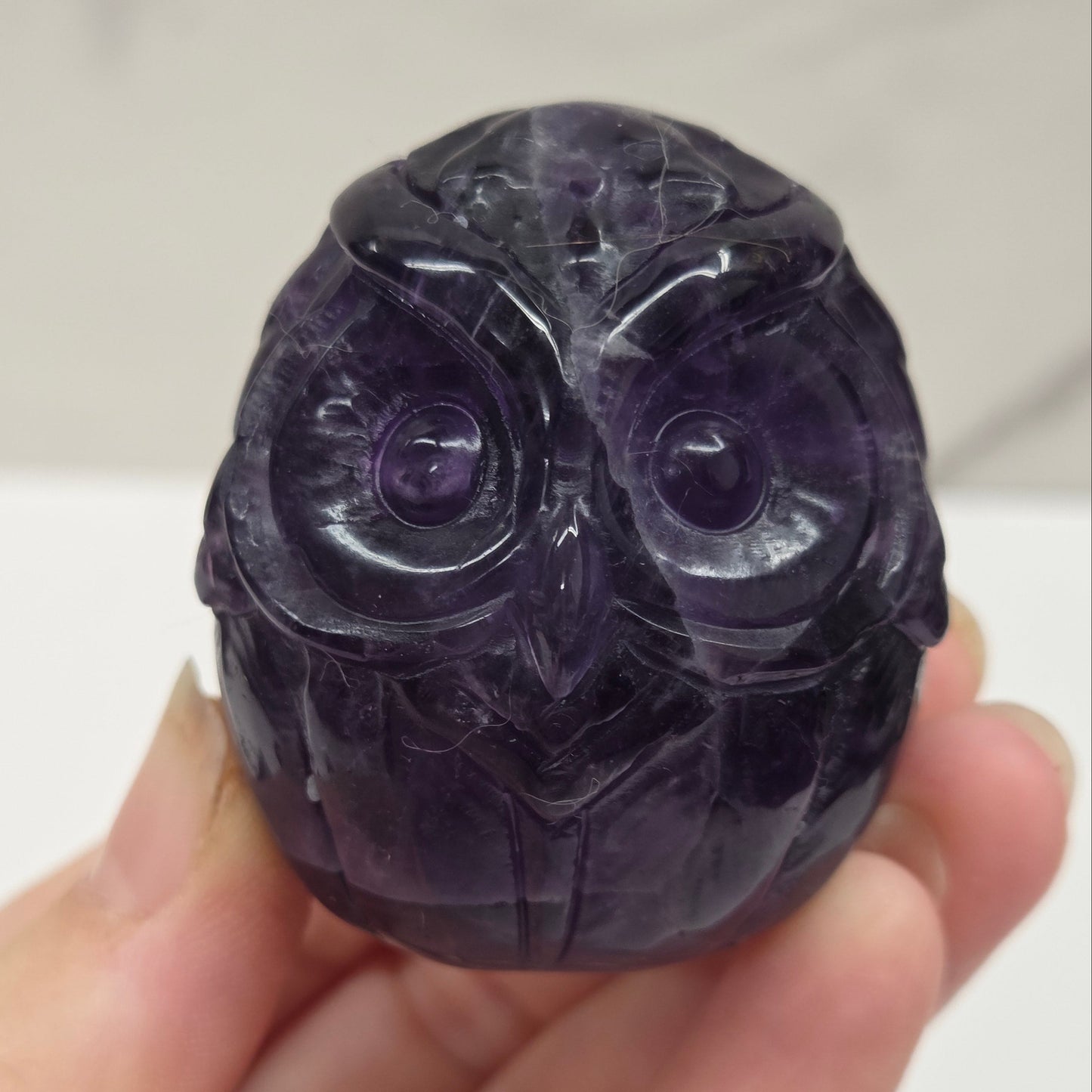 Hand holding a dark purple stone with intricate carvings on a white background