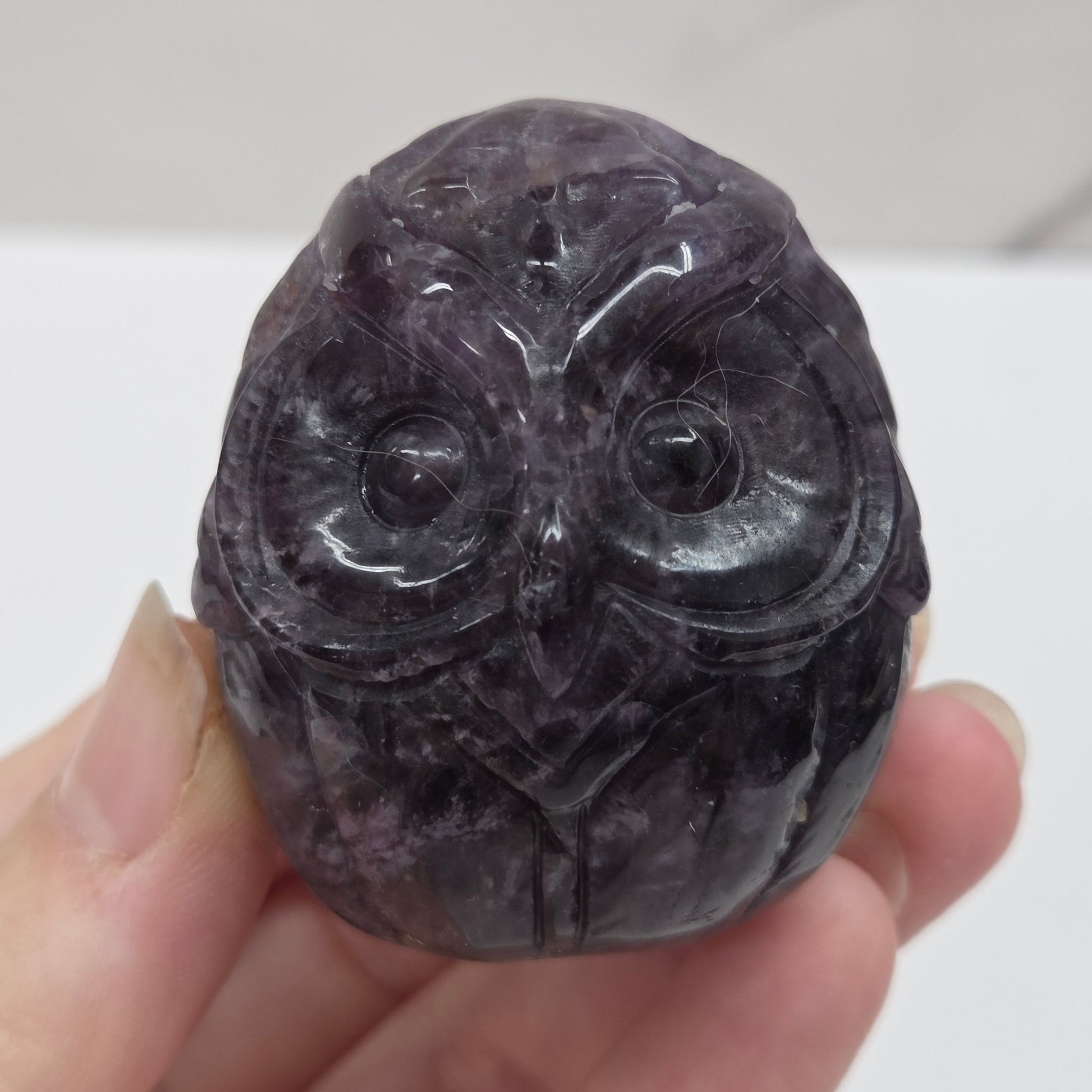 Hand holding a dark stone with intricate carvings against a neutral background