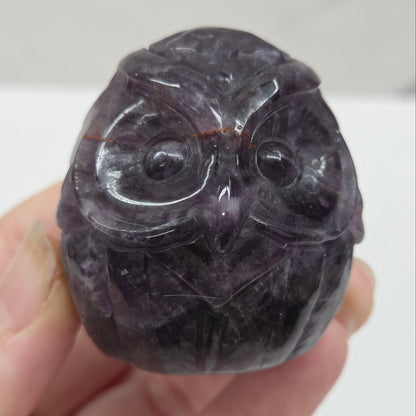 Hand holding a dark purple crystal with intricate carvings against a white background