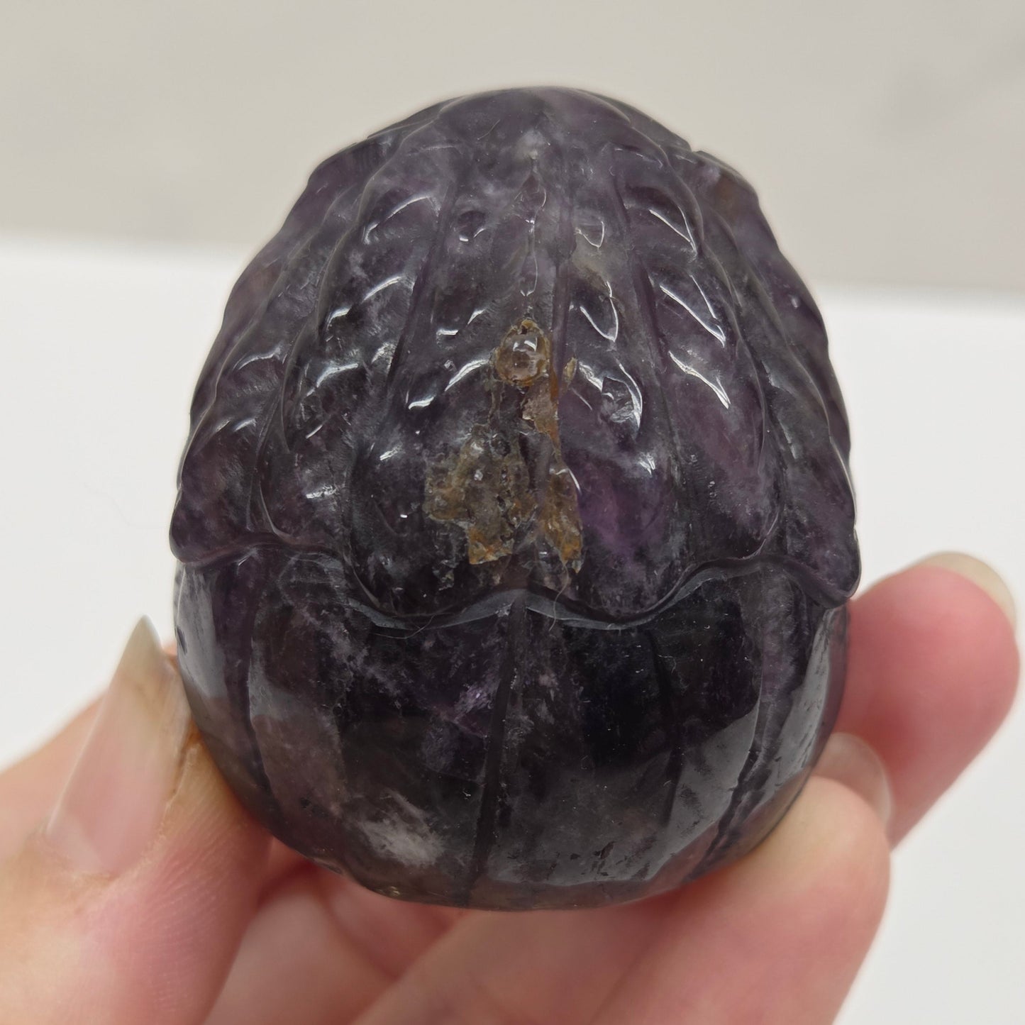 Hand holding a purple stone with intricate patterns against a plain background