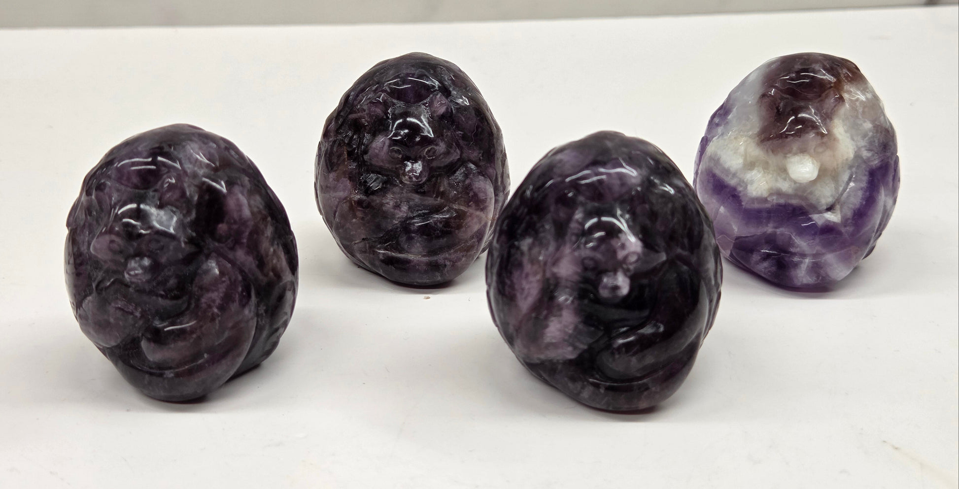 Four amethyst carved stones on a white surface with a marble background