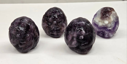 Four amethyst carved stones on a white surface with a marble background