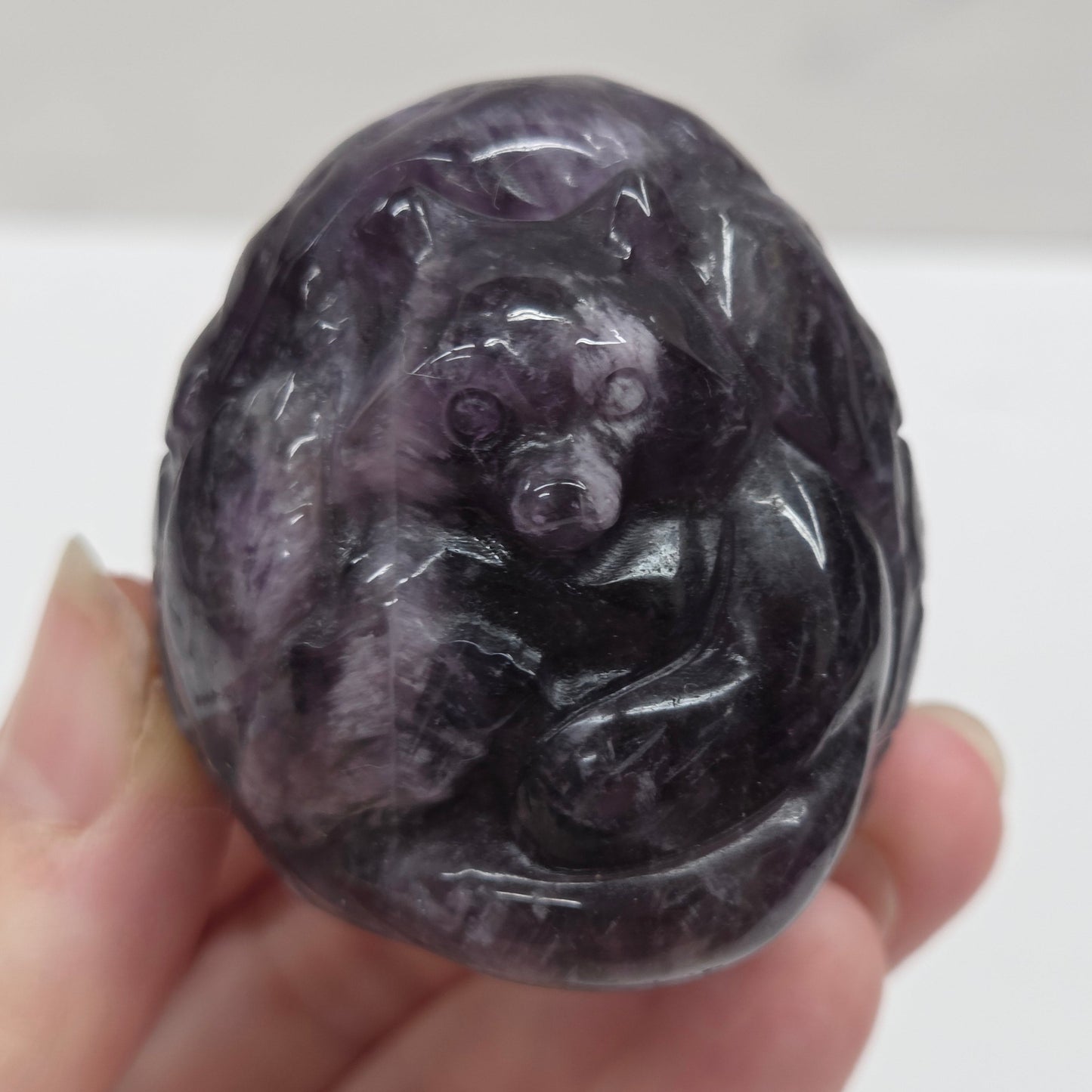 Hand holding a dark purple stone with intricate patterns against a white background