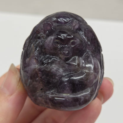 Hand holding a purple stone with a carved design against a white background