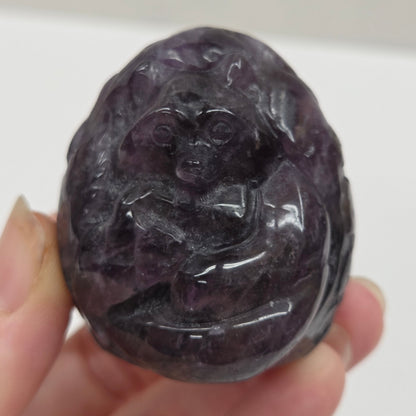 Hand holding a dark purple stone with intricate carvings against a white background