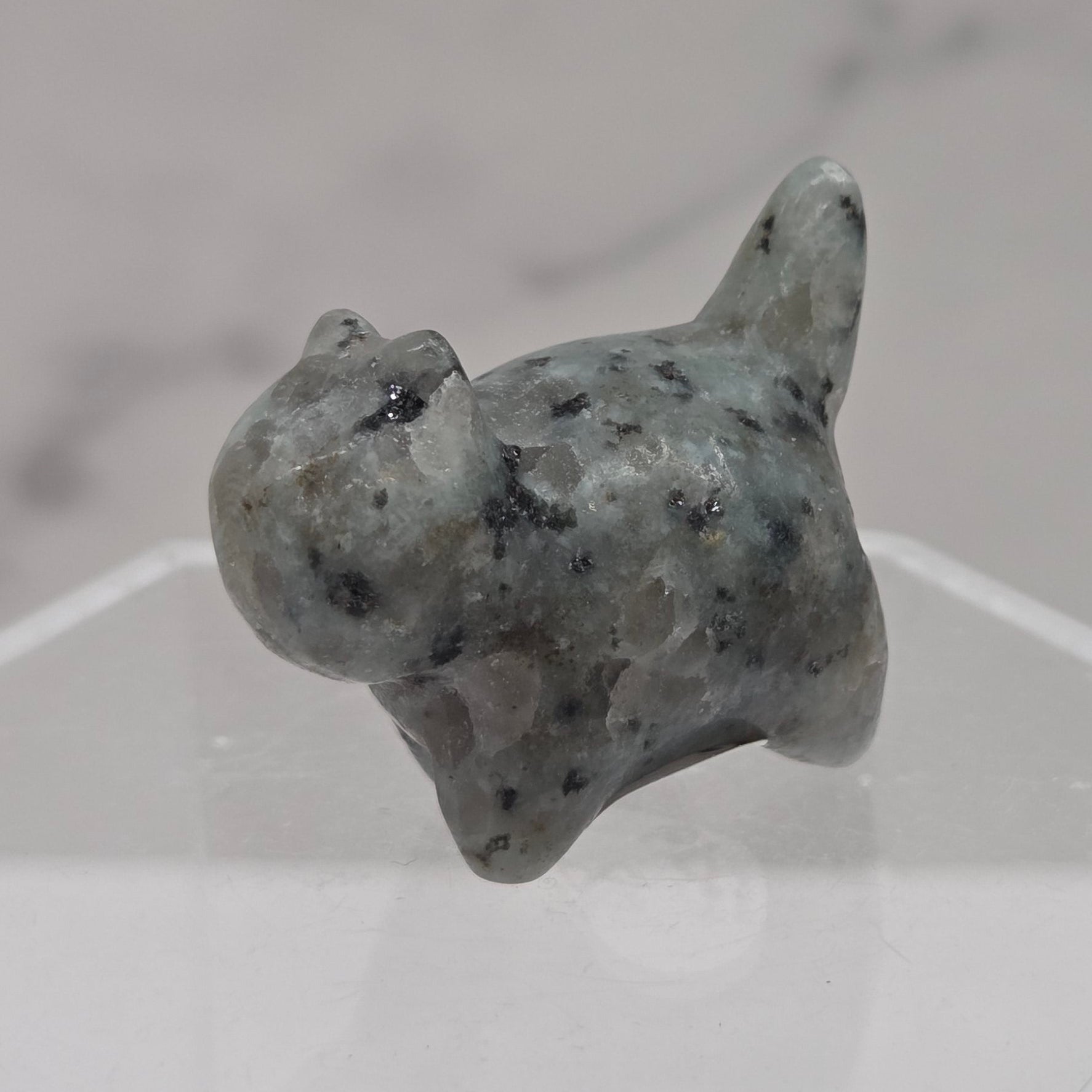 Small stone sculpture of a cat on a hexagonal stand with a marble background