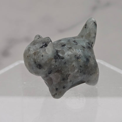 Small stone sculpture of a cat on a hexagonal stand with a marble background