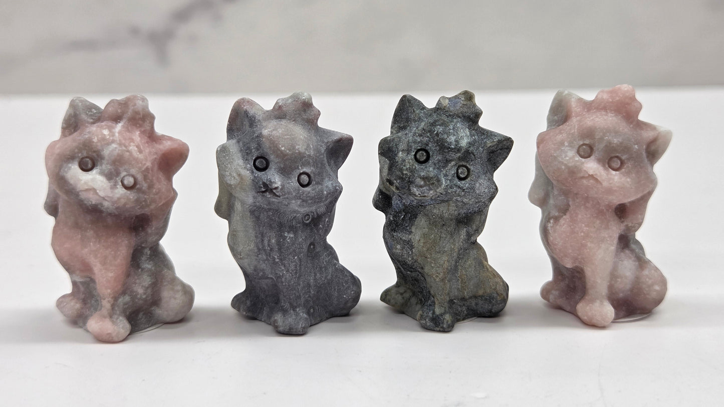 Four small stone cat figurines of different colors on a marble surface