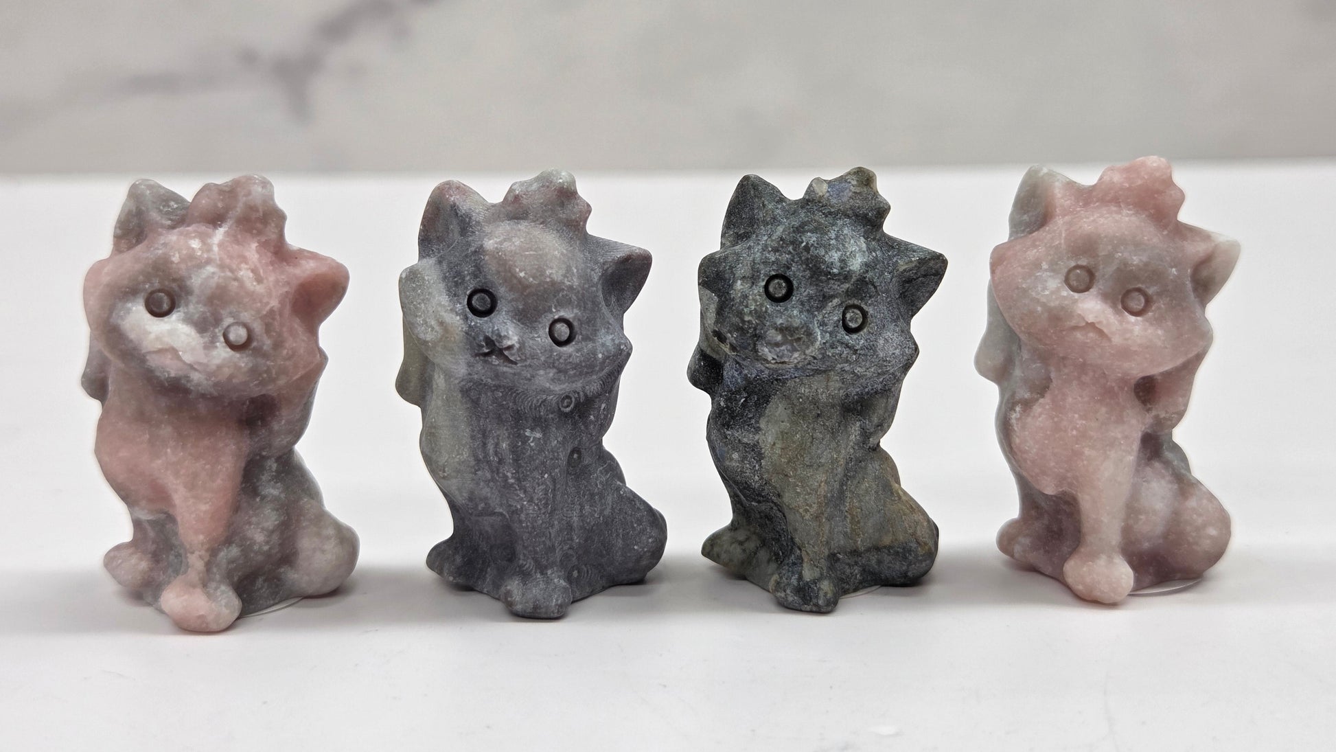 Four small stone cat figurines of different colors on a marble surface