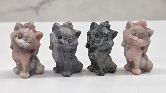 Four small stone cat figurines of different colors on a marble surface