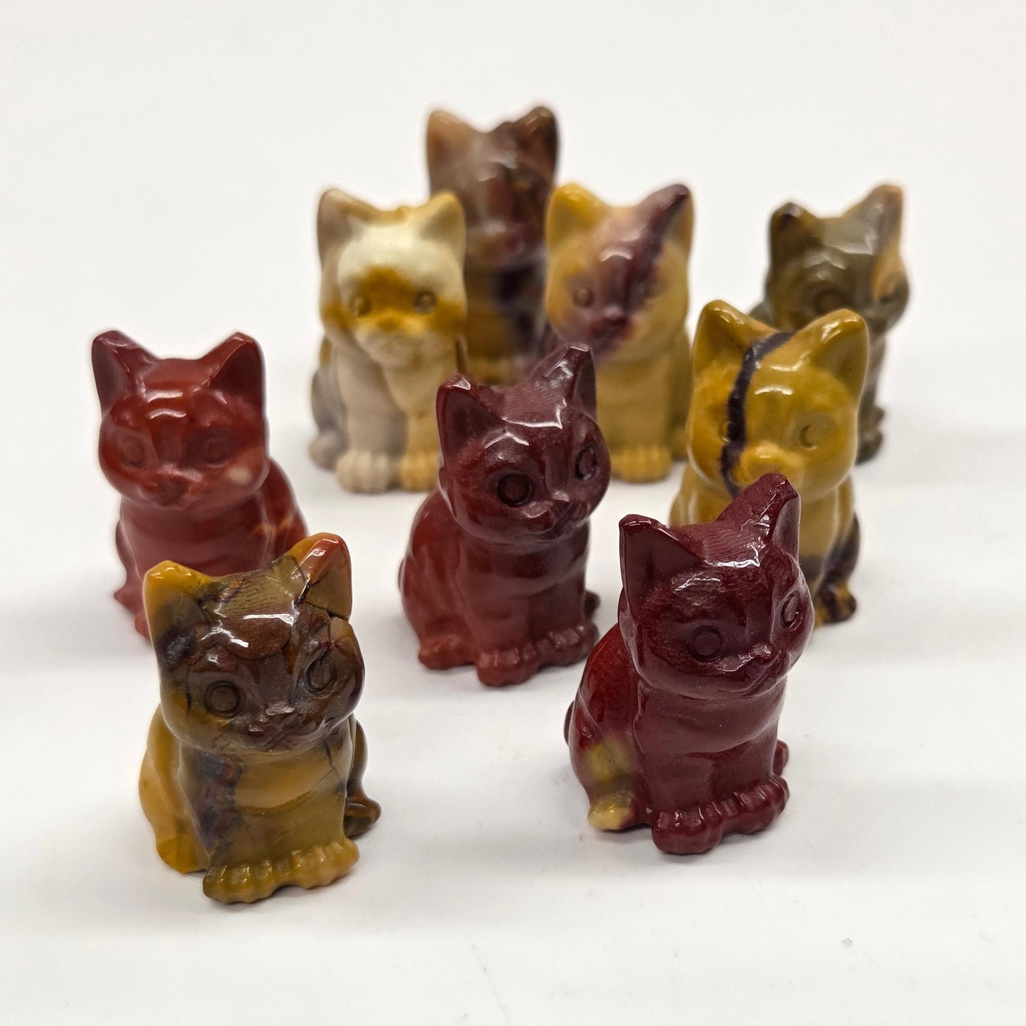 Mookaite cat carvings in red, yellow, and brown on a white background