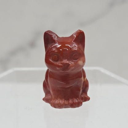 Mookaite cat carving in red, yellow, and brown on a white background