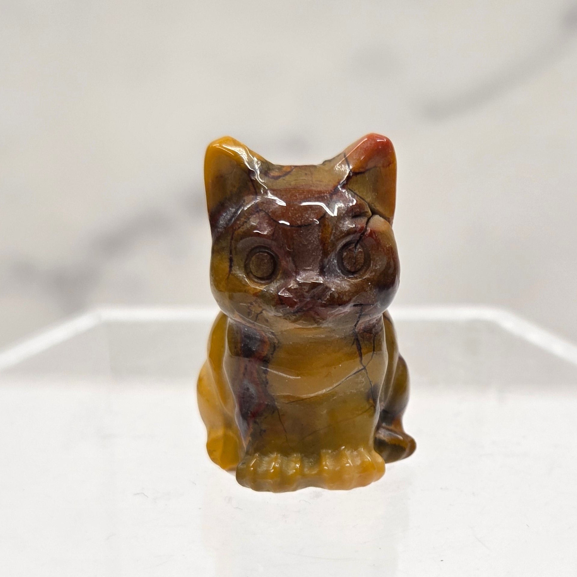Mookaite cat carving in red, yellow, and brown on a white background