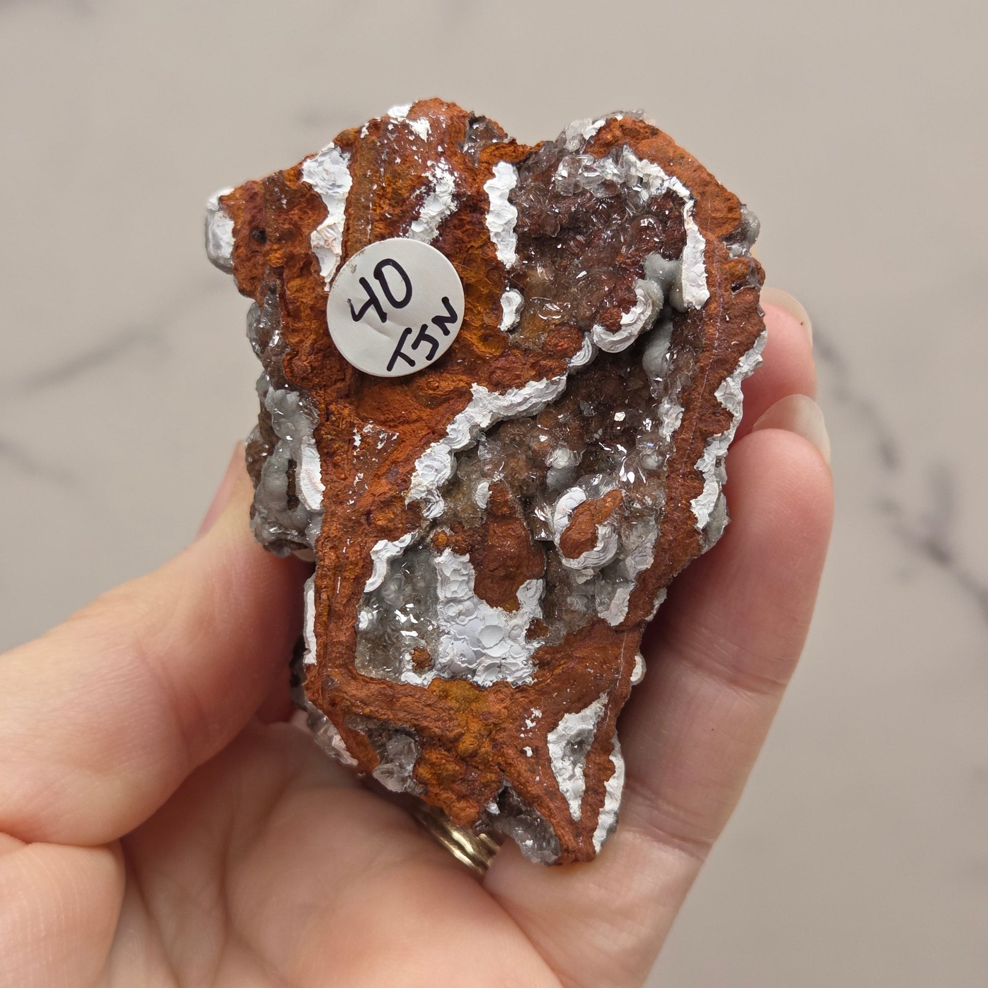 Hand holding a rough mineral specimen with a label against a neutral background