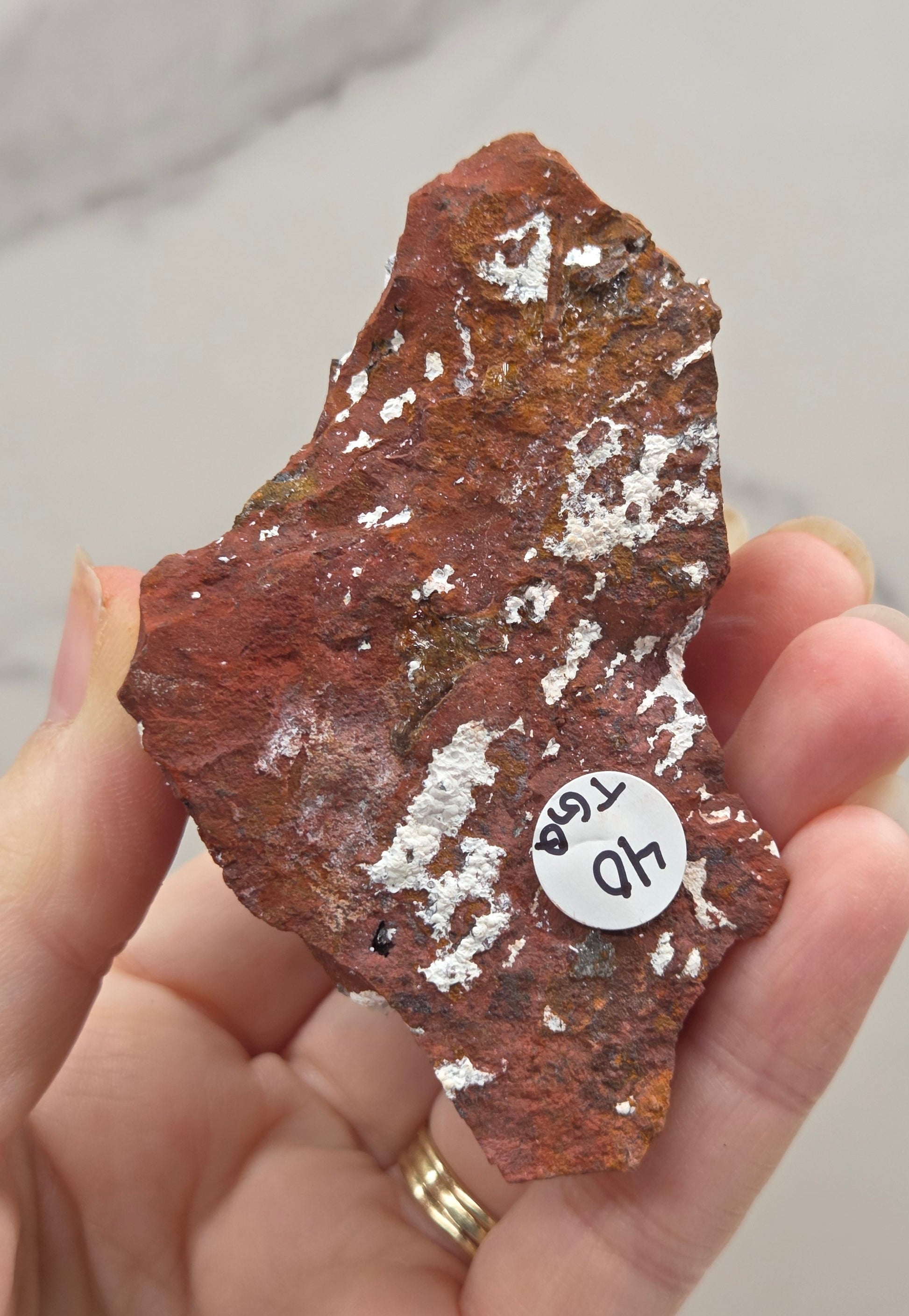 Hand holding a brown mineral specimen with a label on a neutral background