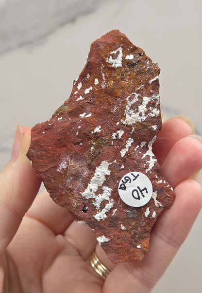 Hand holding a brown mineral specimen with a label on a neutral background