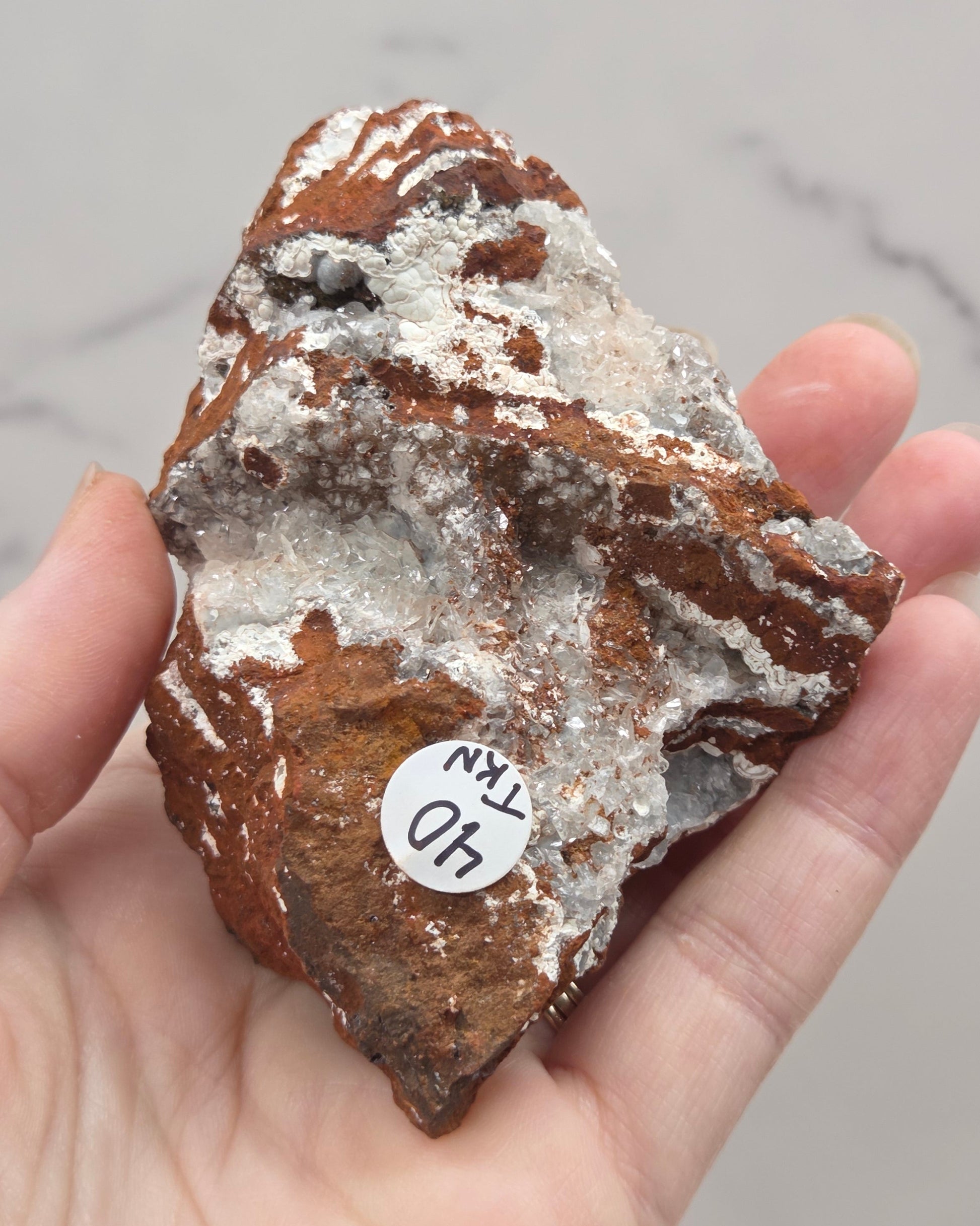 Hand holding a brown mineral specimen with a white label against a marble background