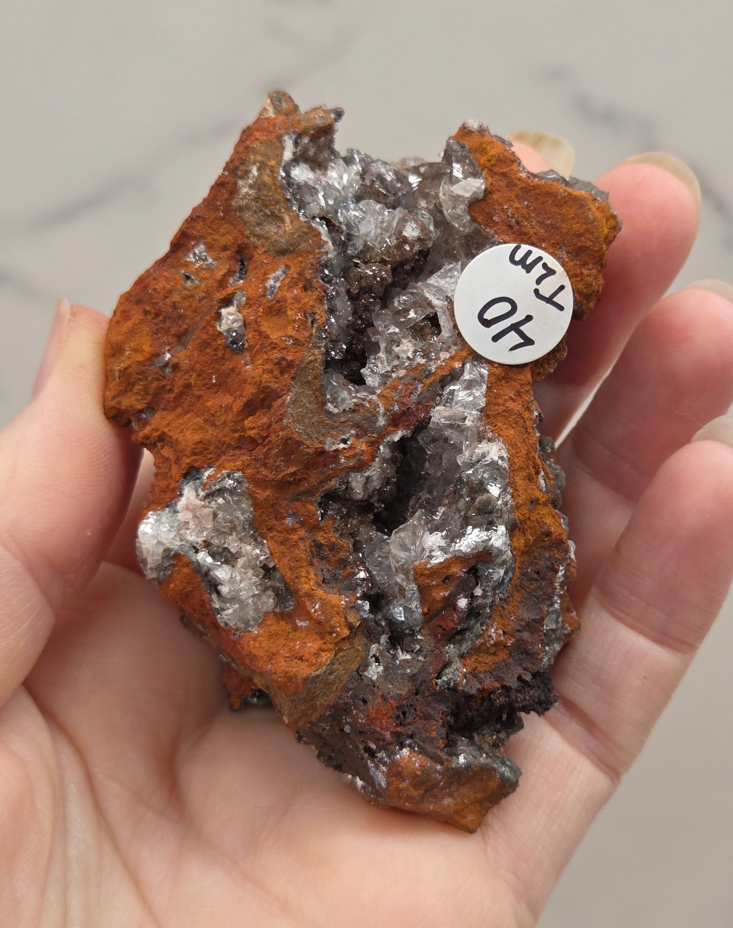Mineral sample held in a hand with a label, against a neutral background