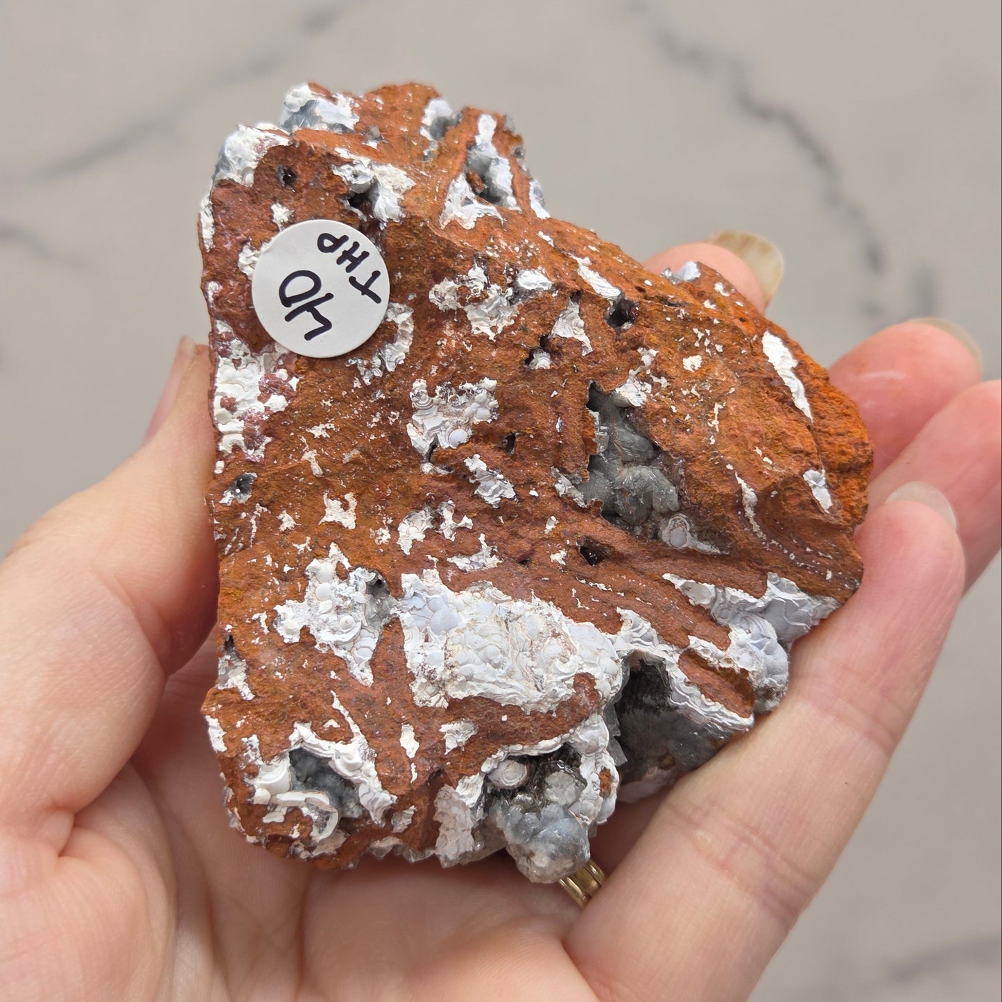 Hand holding a rock with a small white label on a neutral background