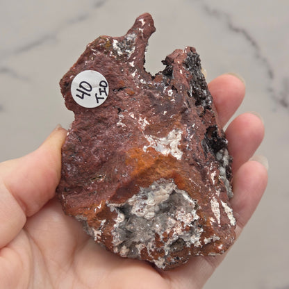 Hand holding a rough mineral specimen with a label on a marble surface