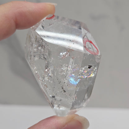Clear Quartz held between fingers against a neutral background