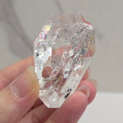 Clear crystal held in a hand against a neutral background