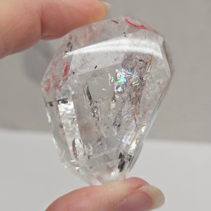 Clear Quartz held between fingers against a neutral background
