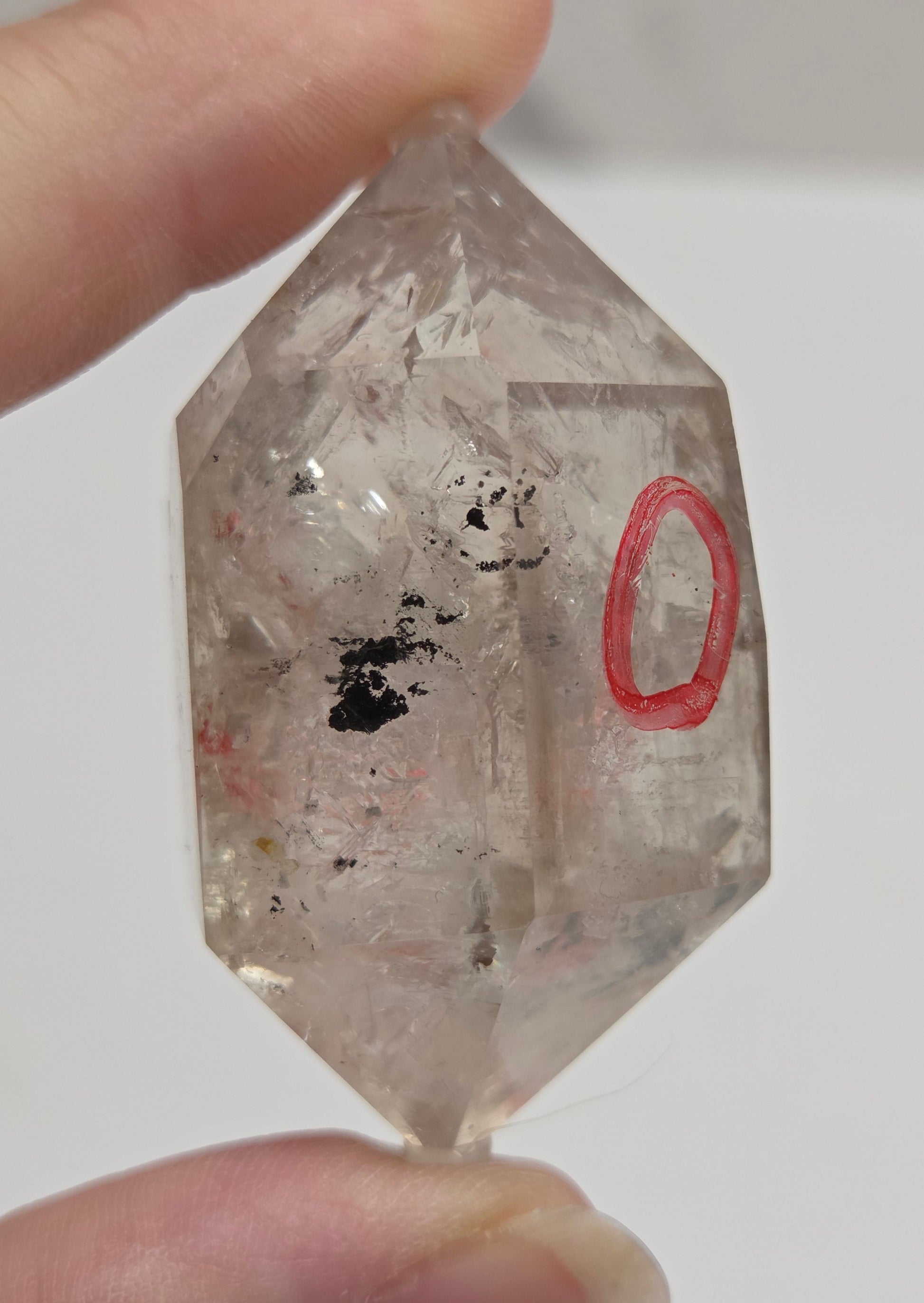 Crystal held between two fingers with a red circle on a white background