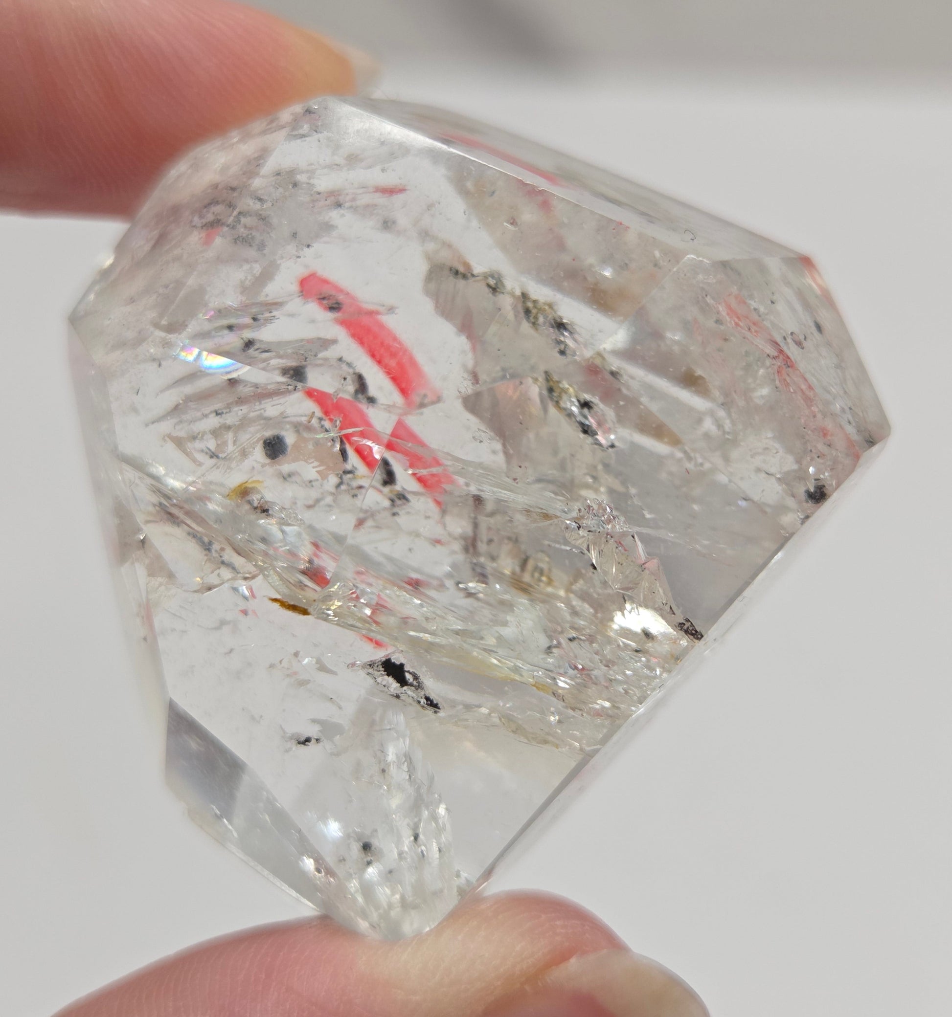 Clear crystal with inclusions held by a hand against a neutral background