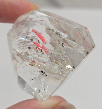 Clear crystal with inclusions held by a hand against a neutral background