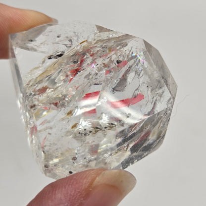 Clear Quartz held between fingers against a neutral background