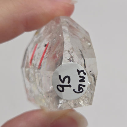 Clear Quartz held between fingers against a neutral background