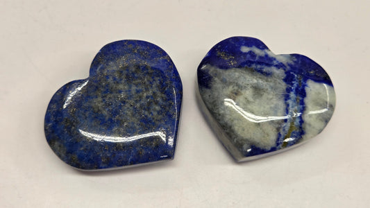 Two heart-shaped lapis lazuli stones on a light gray background