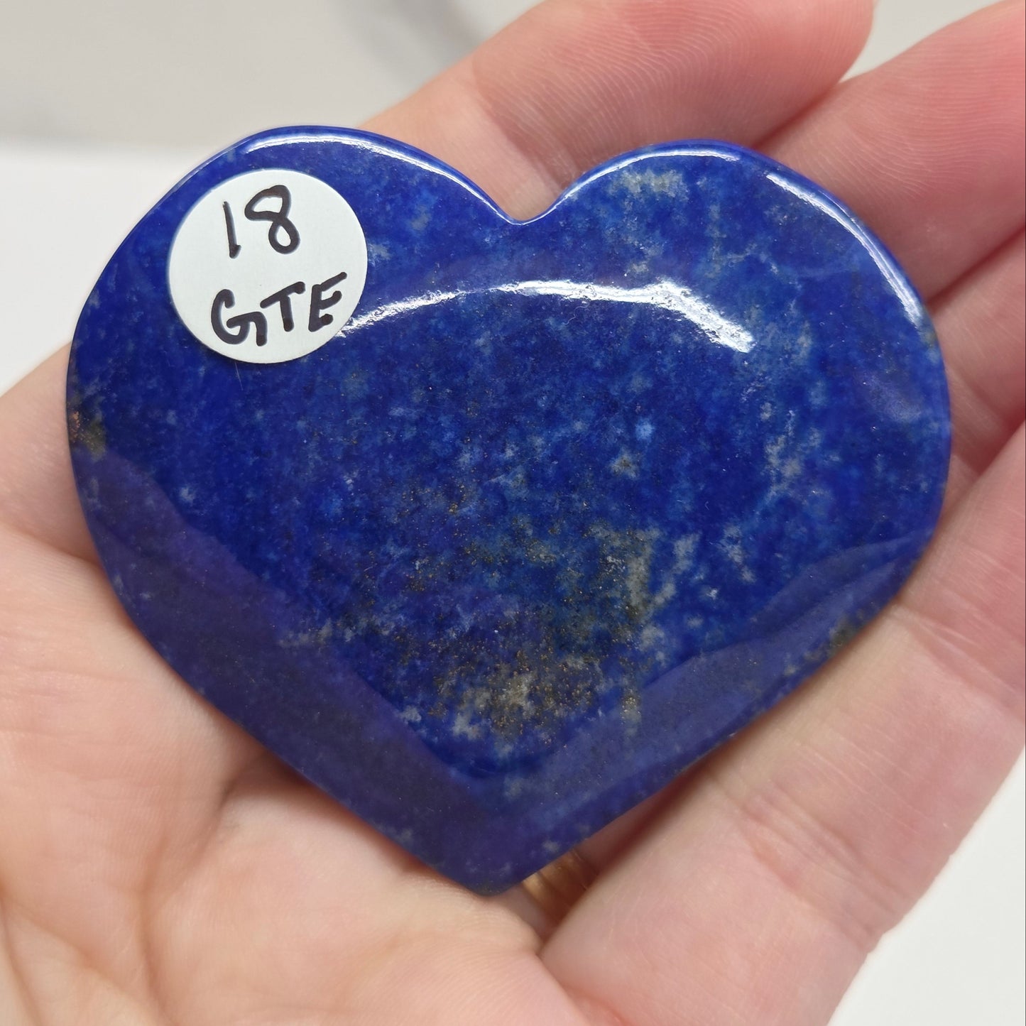 Heart-shaped blue stone held in a hand with a label on a white background