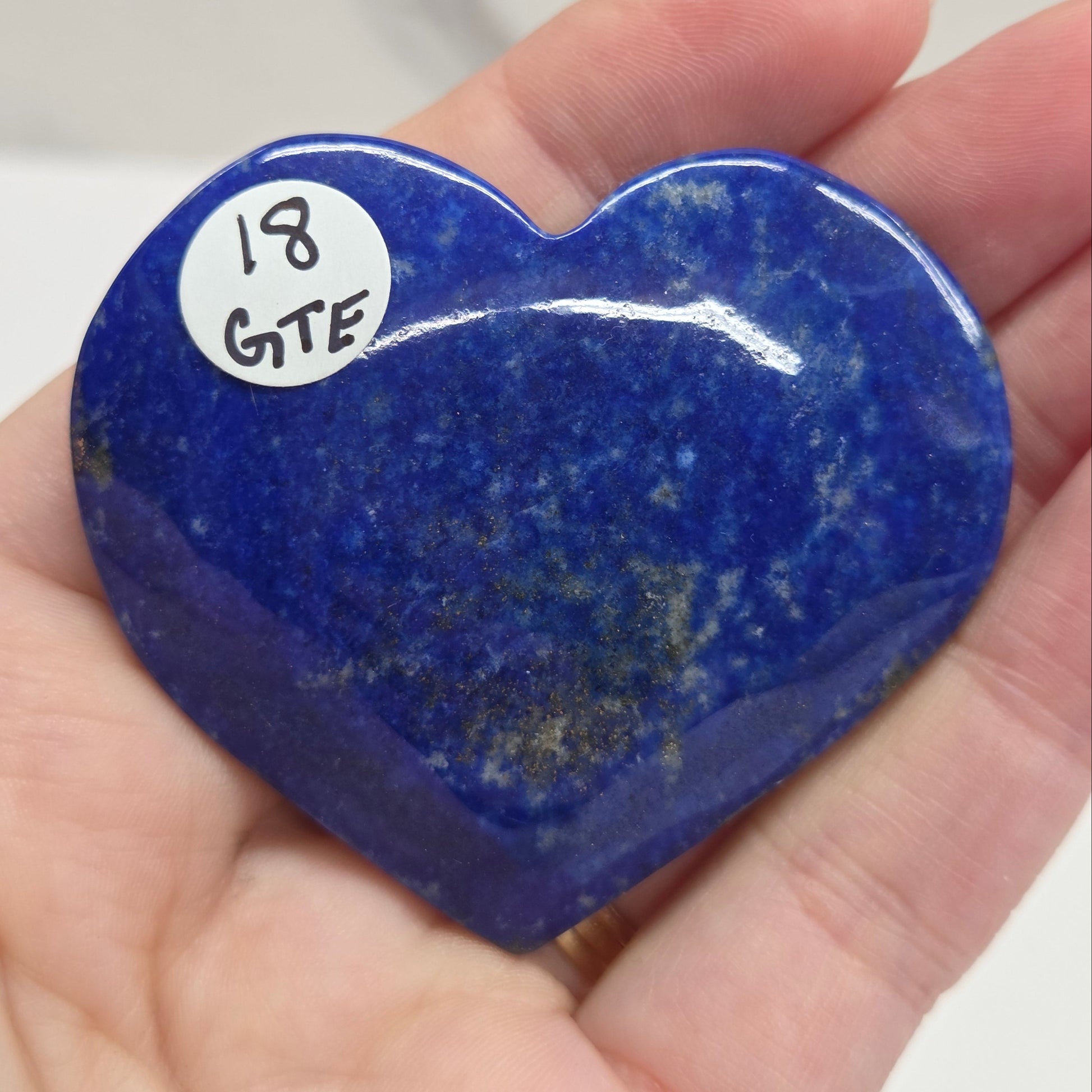 Heart-shaped blue stone held in a hand with a label on a white background