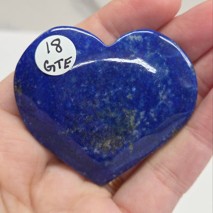 Heart-shaped blue stone held in a hand with a label on a white background