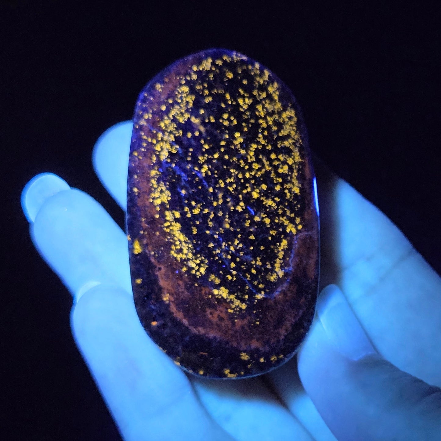 Hand holding a glowing stone with yellow specks under a black light