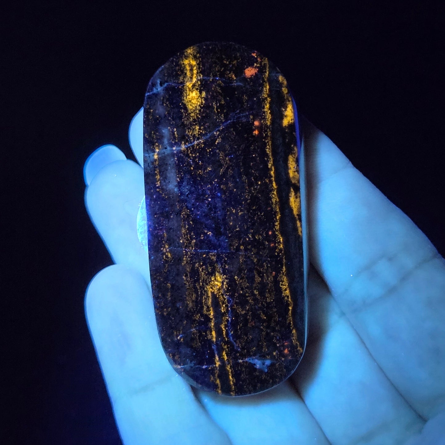 Hand holding a dark stone with glowing yellow patterns against a black background